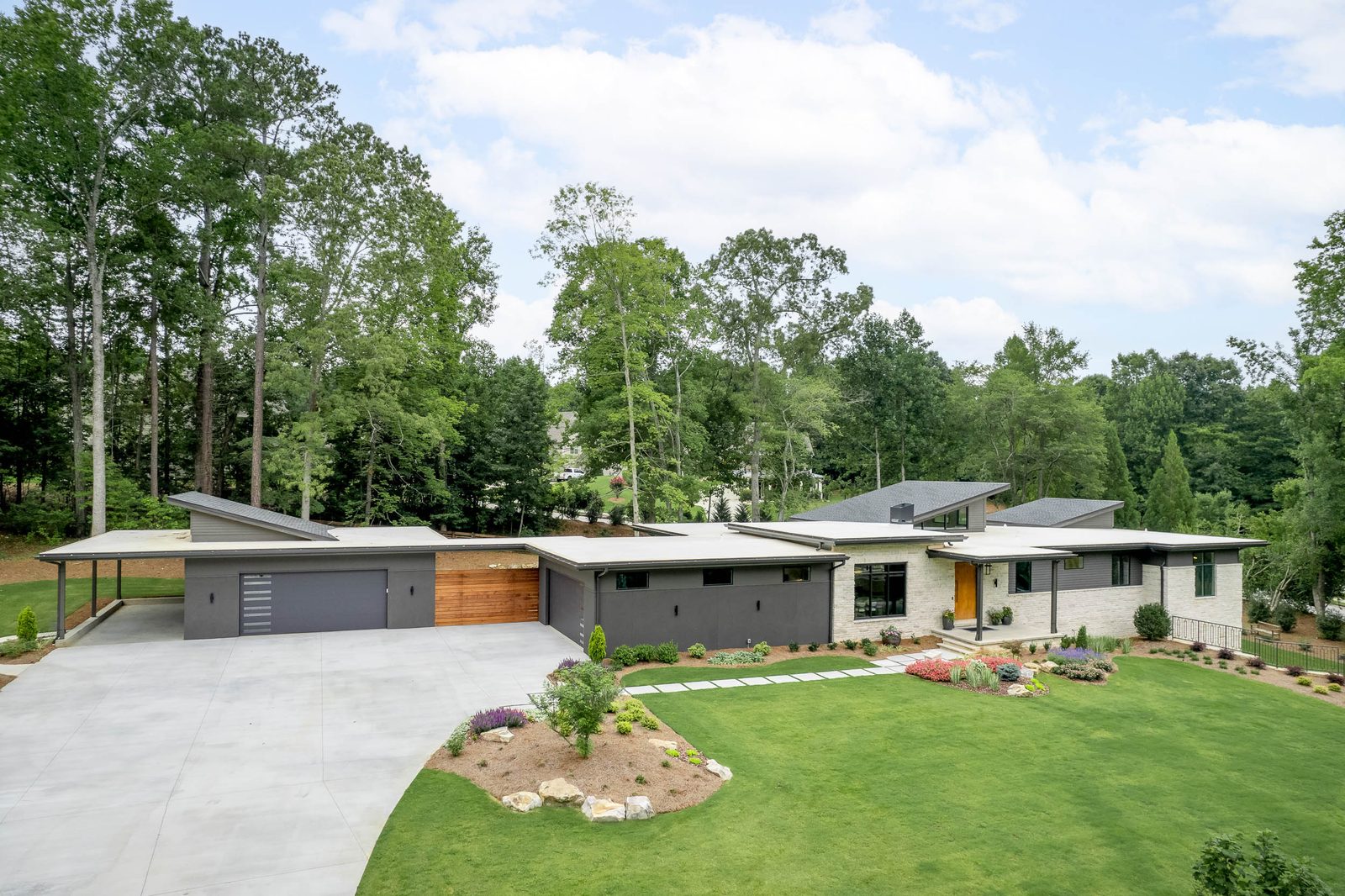 Wide view of the drive court and garage wing among the trees — The Ortiz Home, custom home built by Ironwood Construction Group in Sugar Hill, Georgia