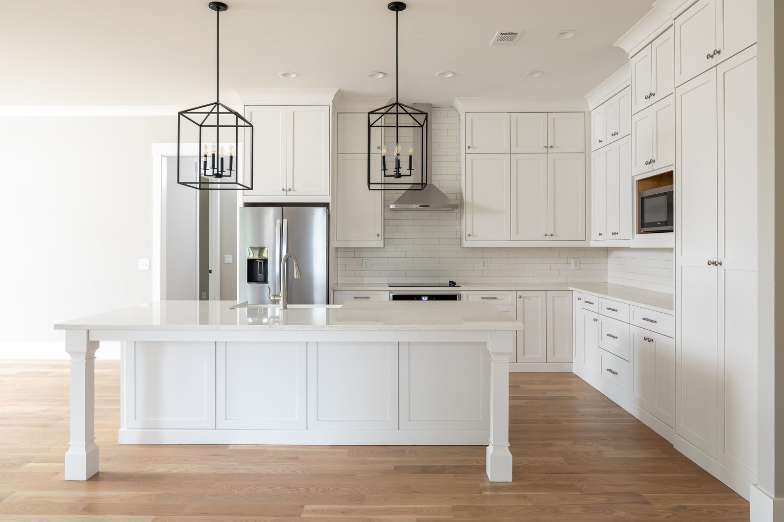 Kitchen with white cabinetry, quartz island and lantern pendants — Shadburn Ferry, custom home built by Ironwood Construction Group in Buford, Georgia