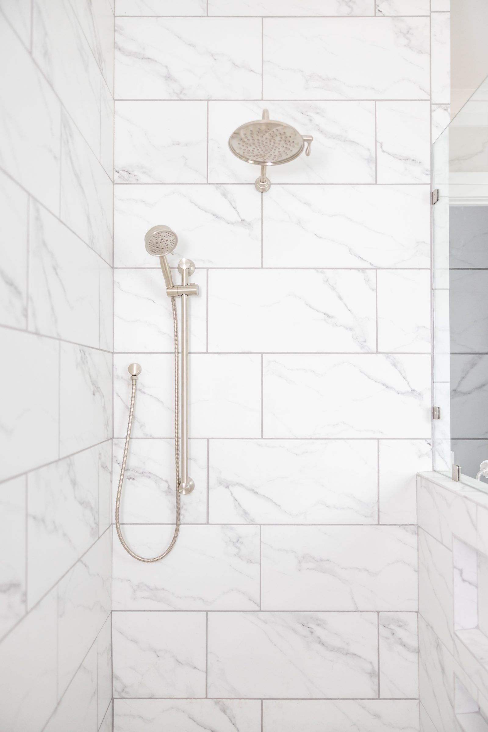Marble-tiled walk-in shower with rain head and hand shower — Shadburn Ferry, custom home built by Ironwood Construction Group in Buford, Georgia
